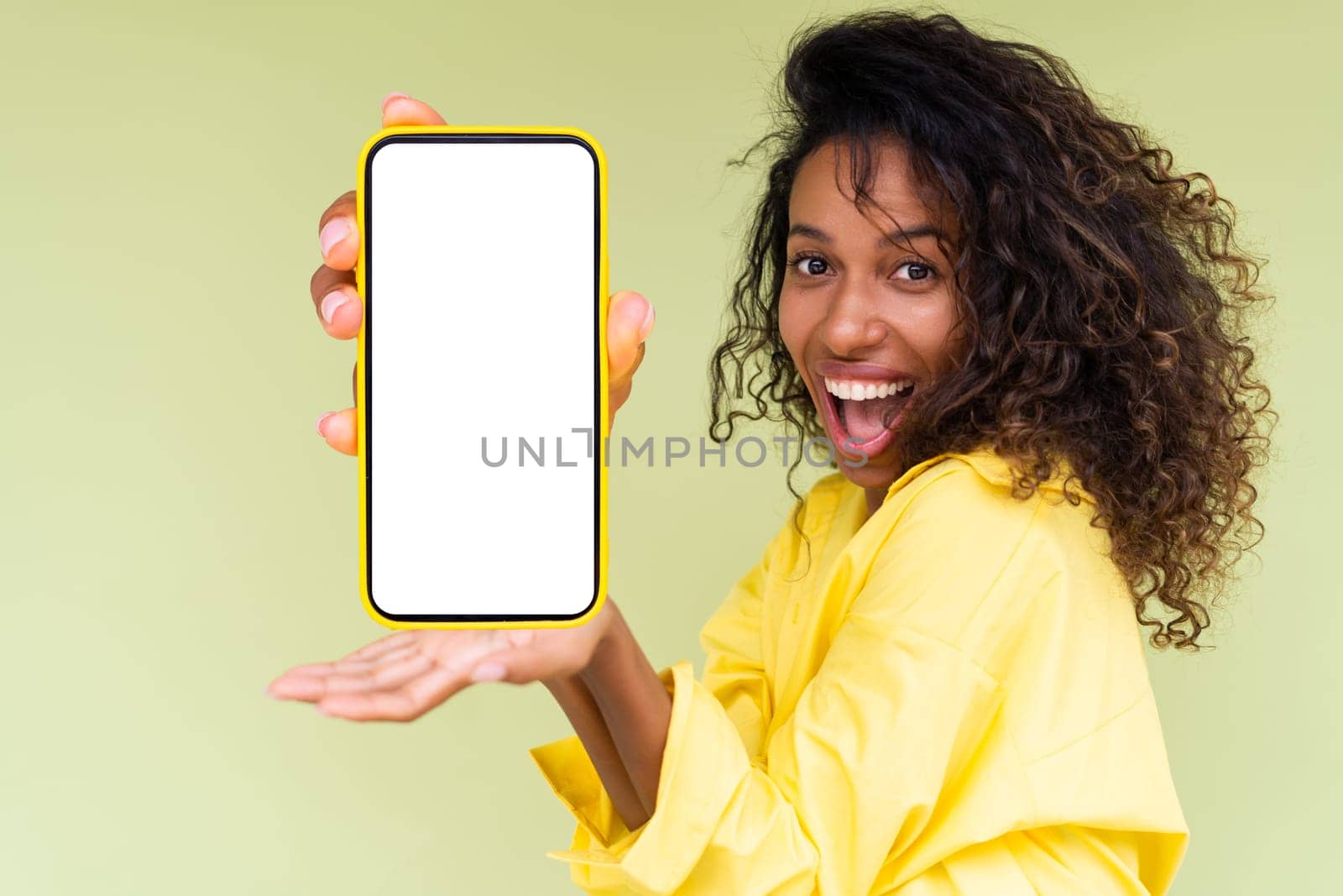 Beautiful african american woman in casual shirt on green background holds a phone with a blank white screen by kroshka_nastya