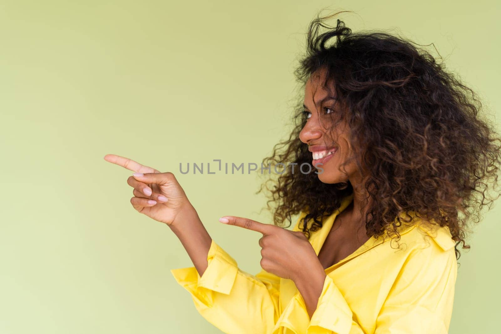 Beautiful african american woman in casual shirt on green background happy positive excited point finger to the left