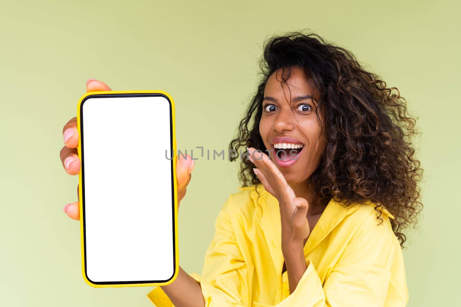 Beautiful african american woman in casual shirt on green background holds a phone with a blank white screen by kroshka_nastya