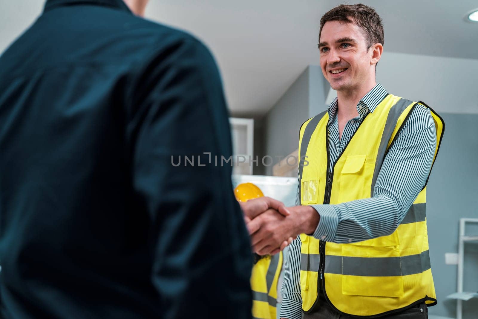 An engineer with a protective vest handshake with an investor in his office. Following a successful meeting, employee and employer form a partnership.