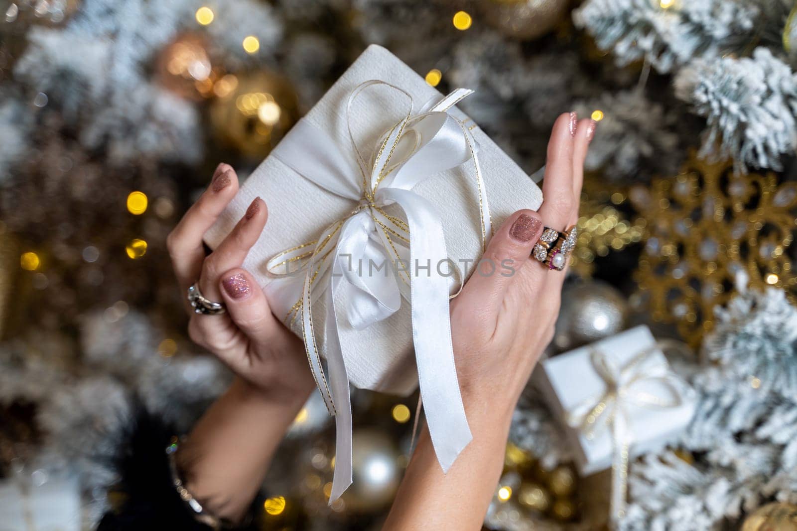 Female hands hold a gift box tied with a ribbon on the background of a Christmas tree, the concept of christmas and gifts
