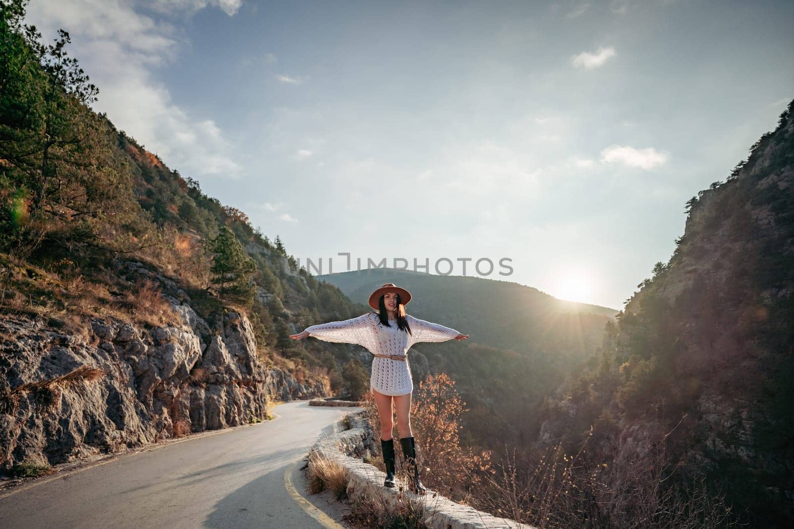 Woman road mountain. A woman in a white sweater, black boots and a hat walks along a winding alpine path between the mountains at sunset in late summer. The concept of travel. by Matiunina