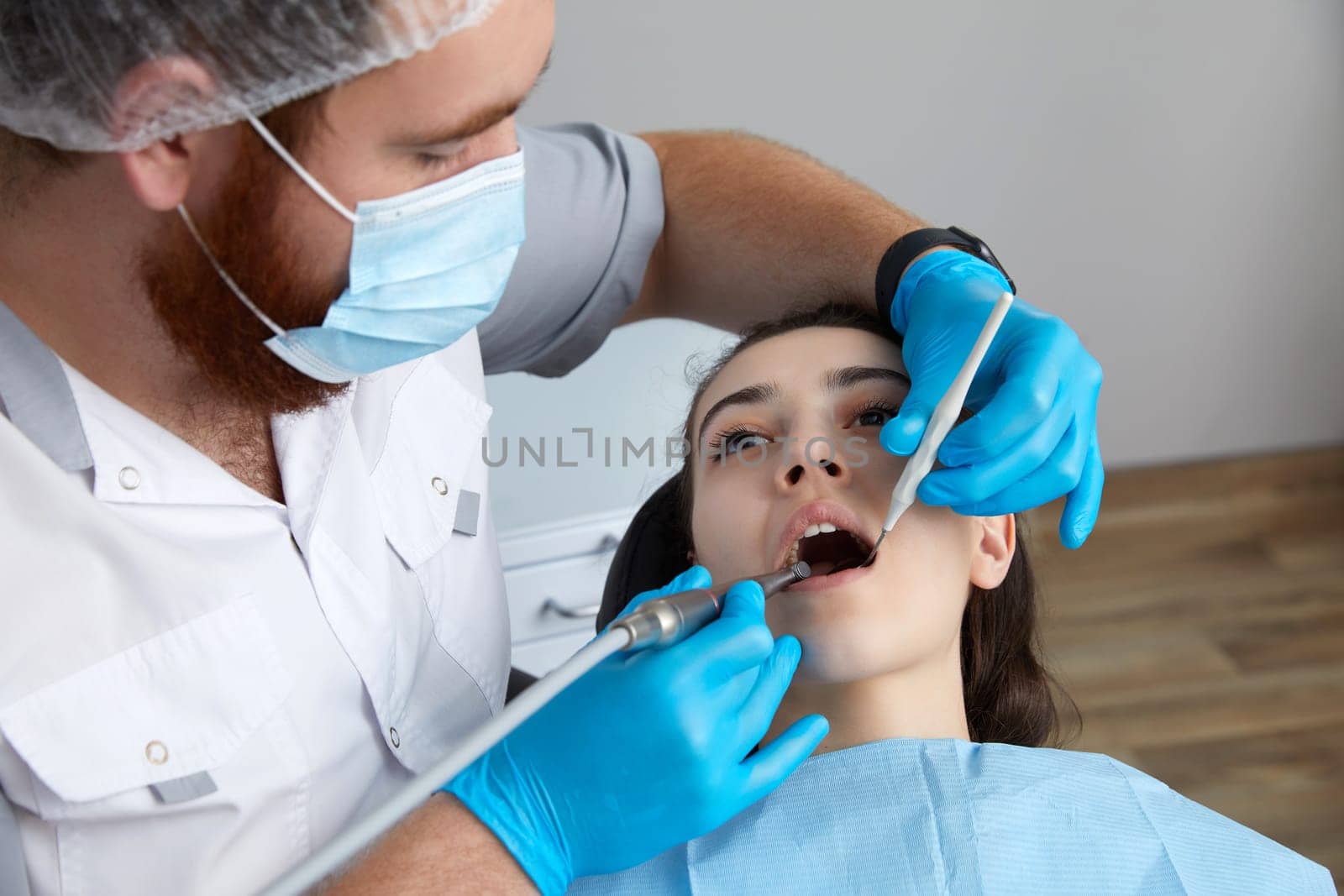 Dentist drilling tooth of female patient in dental chair by Mariakray