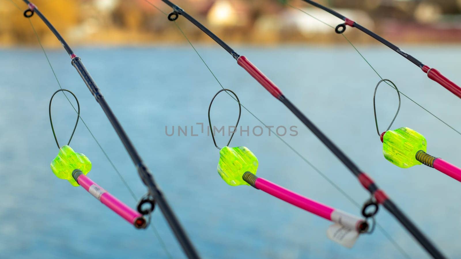 The bite alarm hangs on a fishing rod against the background of water. Fishing rod while fishing on the lake, river. Fishing tackle. Carp rod on a stand with a bite alarm on the line