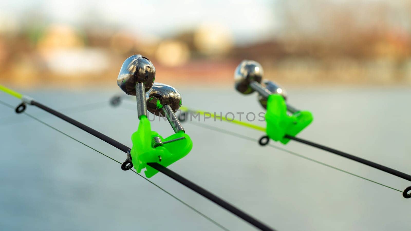 The bite alarm hangs on the tip of the fishing rod against the background of water. Fishing rod while fishing on the lake, river. Fishing tackle. Two rods with bite alarm
