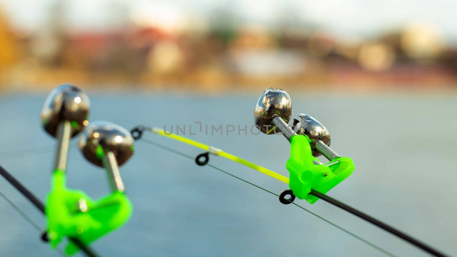 The bite alarm hangs on the tip of the fishing rod against the background of water. Fishing rod while fishing on the lake, river. Fishing tackle. Two rods with bite alarm