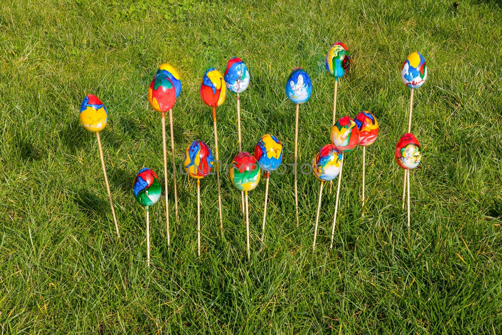 Painted colorful Easter eggs on wooden skewers in green grass