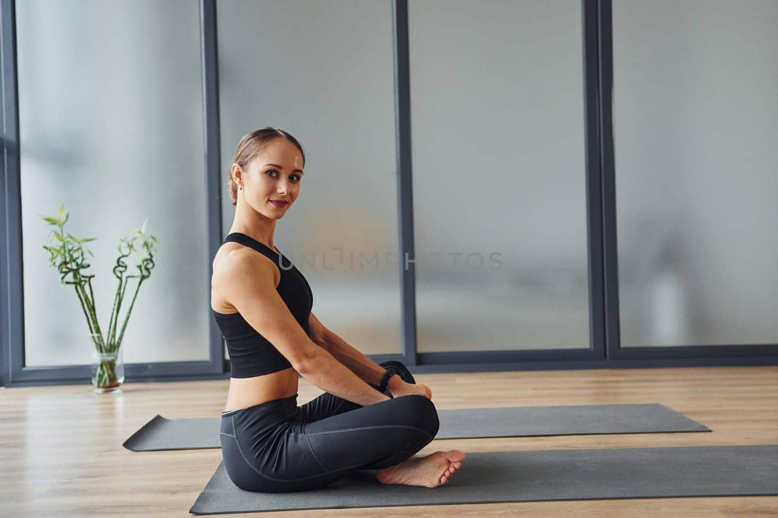 Sits on the mat. Young woman in sportive wear and with slim body have fitness yoga day indoors by Standret