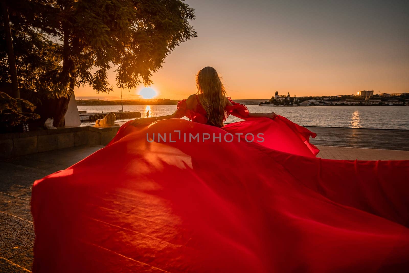 Sunrise red dress. A woman in a long red dress against the backdrop of sunrise, bright golden light of the sun's rays. The concept of femininity, harmony. by Matiunina