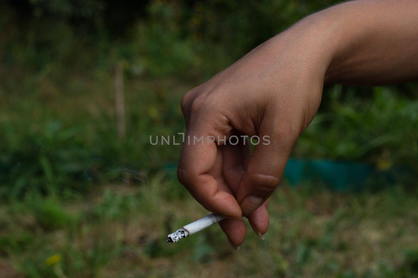 A woman hand is holding a cigarette on the street. The harm of smoking is health care.