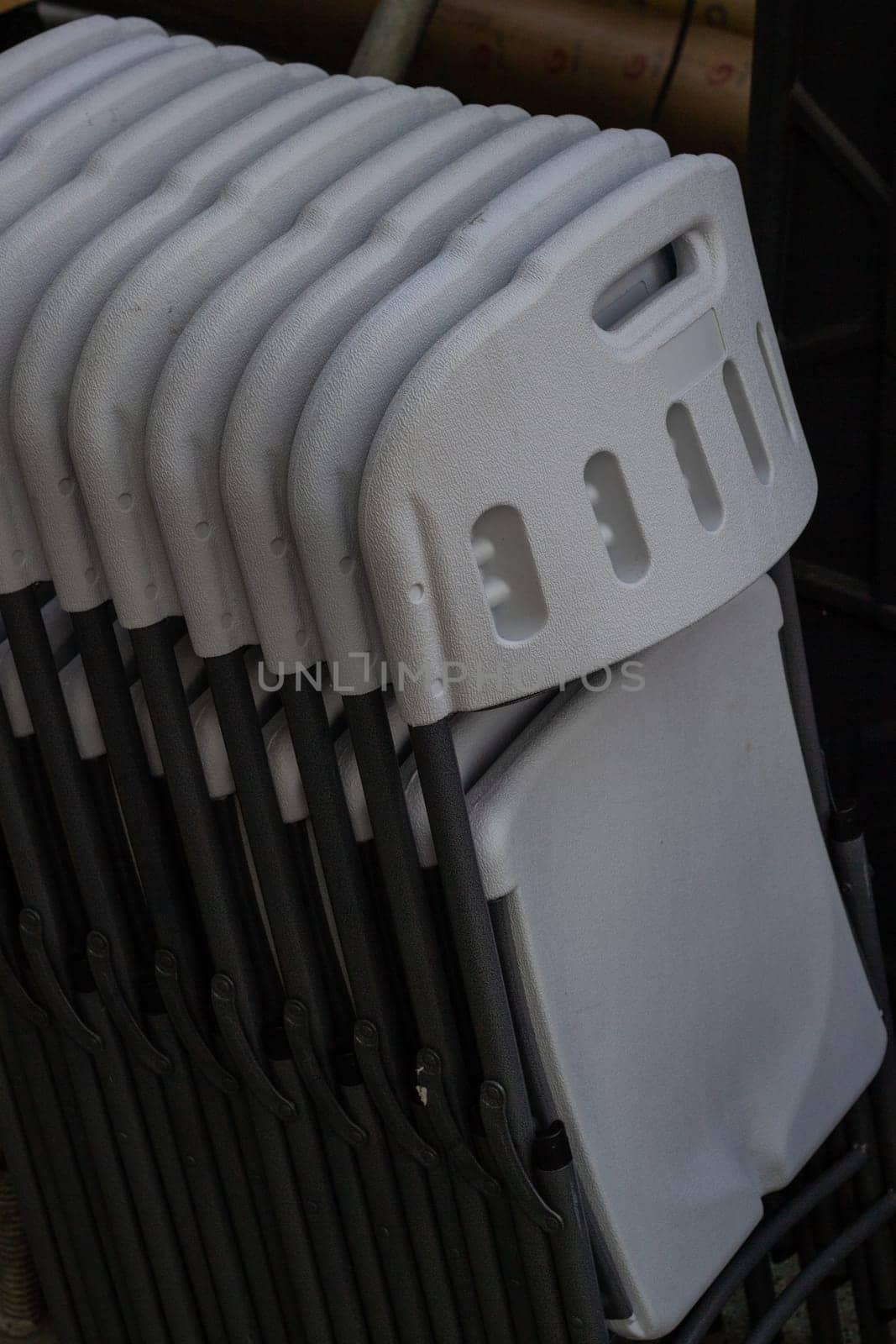 Plastic folding chairs are white stacked on top of each other. Mass events. Outdoor furniture.