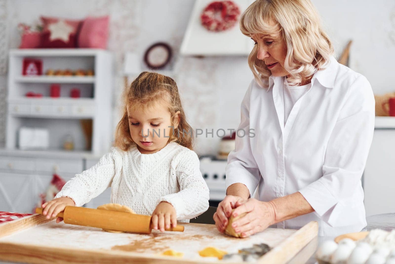 Kneads the dough. Senior grandmother with her little granddaughter cooks sweets for Christmas on the kitchen.