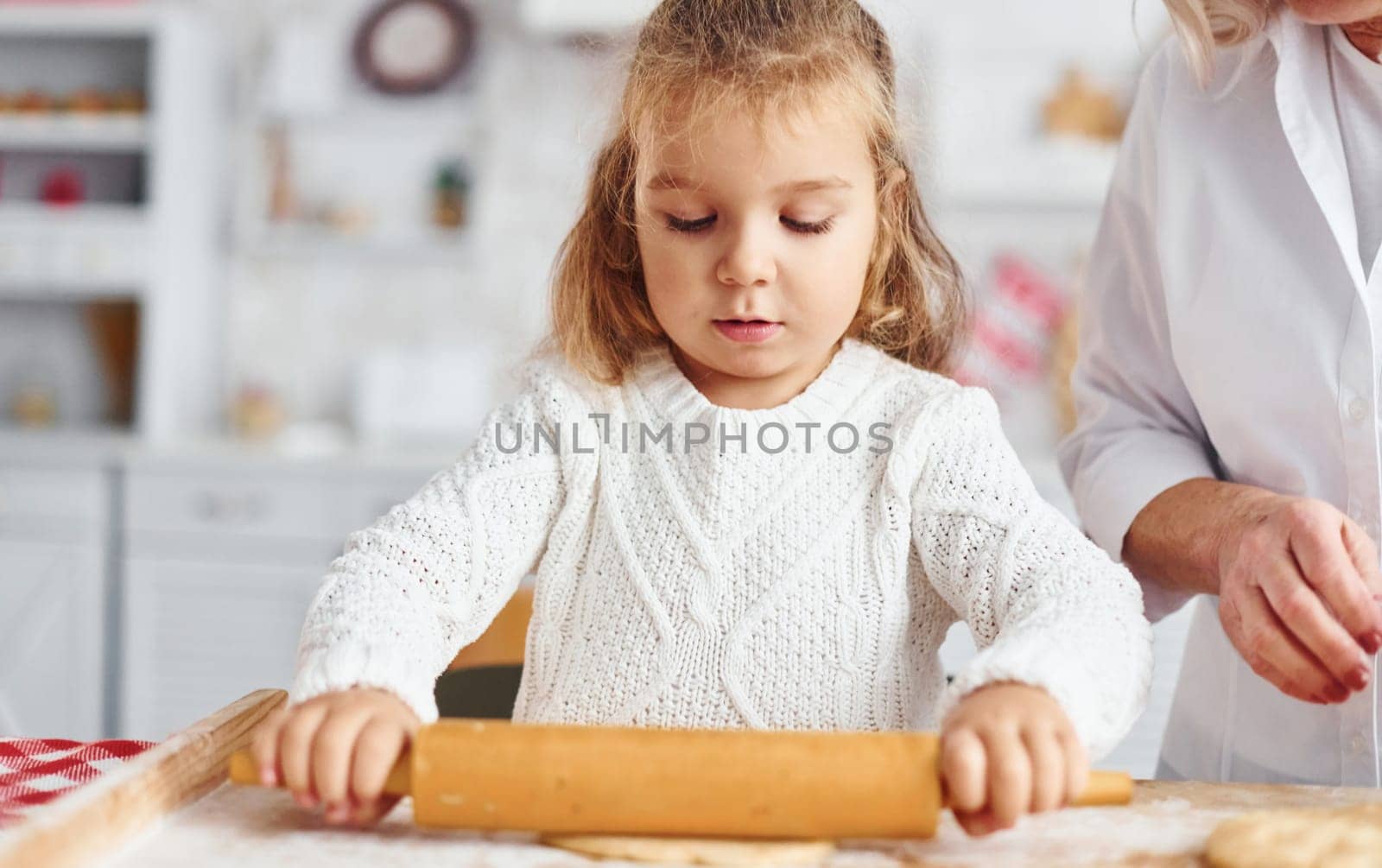 Kneads the dough. Senior grandmother with her little granddaughter cooks sweets for Christmas on the kitchen.