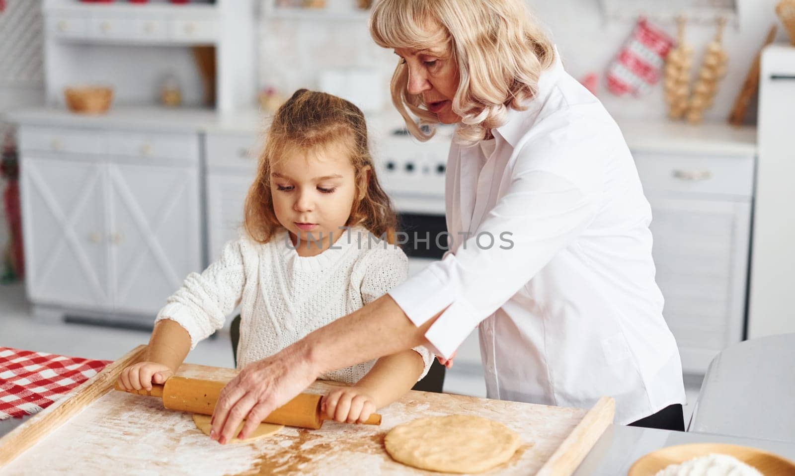 Kneads the dough. Senior grandmother with her little granddaughter cooks sweets for Christmas on the kitchen.