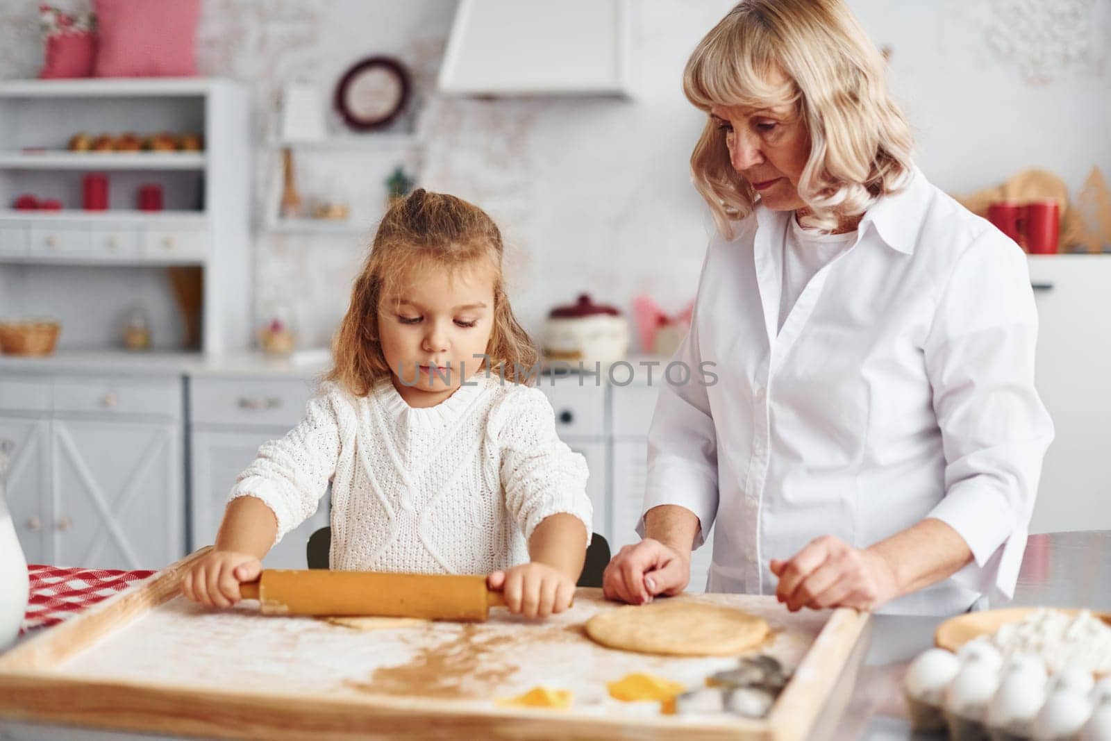 Kneads the dough. Senior grandmother with her little granddaughter cooks sweets for Christmas on the kitchen.