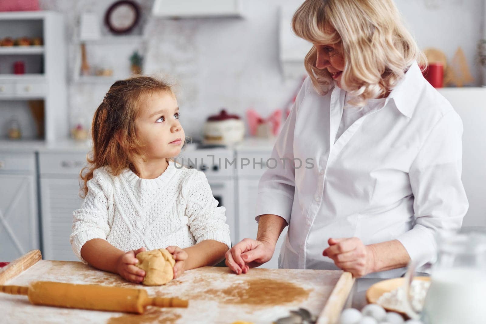 Kneads the dough. Senior grandmother with her little granddaughter cooks sweets for Christmas on the kitchen.
