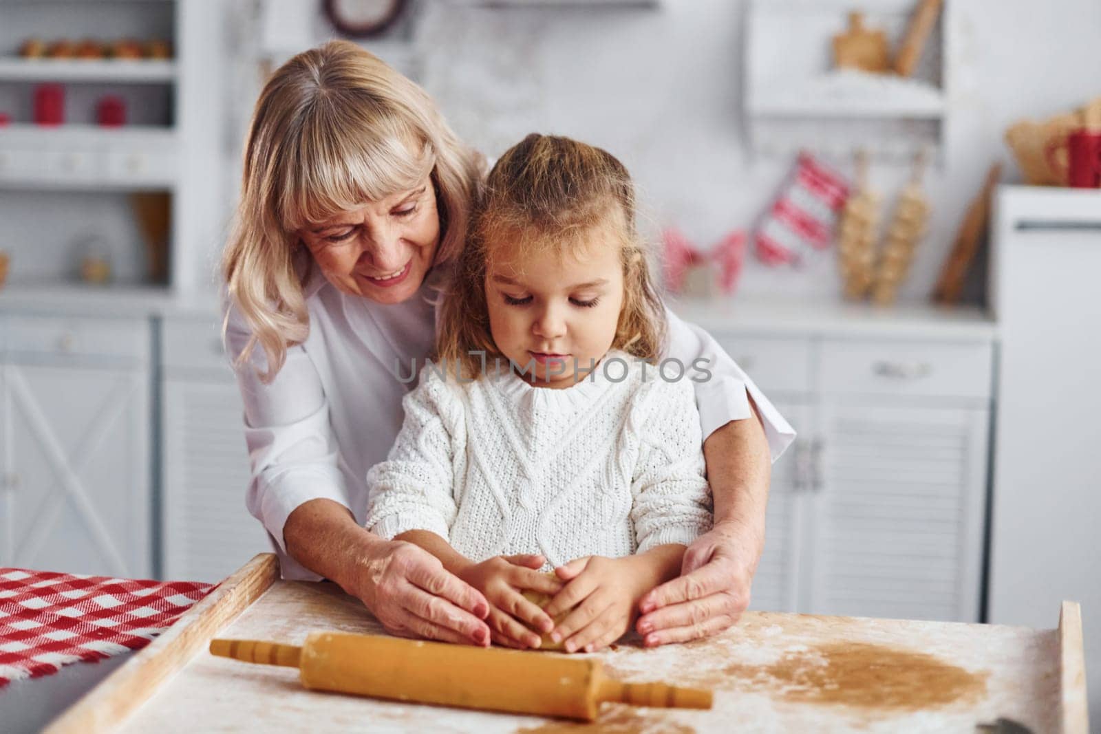 Kneads the dough. Senior grandmother with her little granddaughter cooks sweets for Christmas on the kitchen.