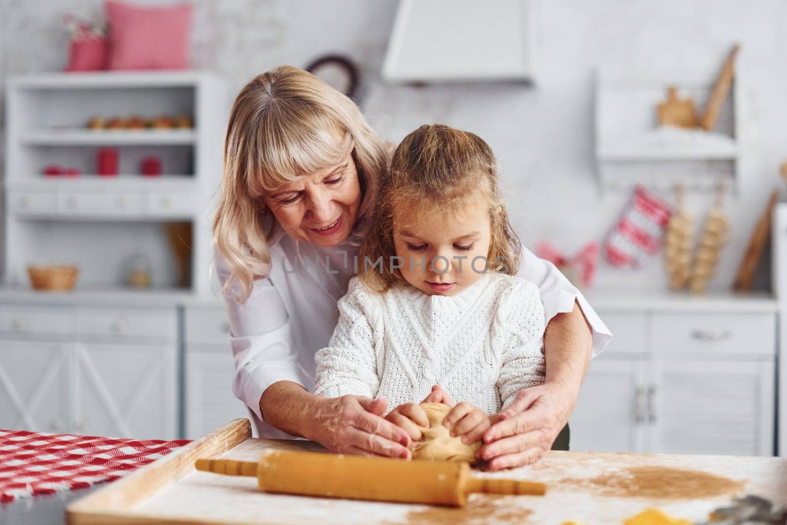 Kneads the dough. Senior grandmother with her little granddaughter cooks sweets for Christmas on the kitchen.