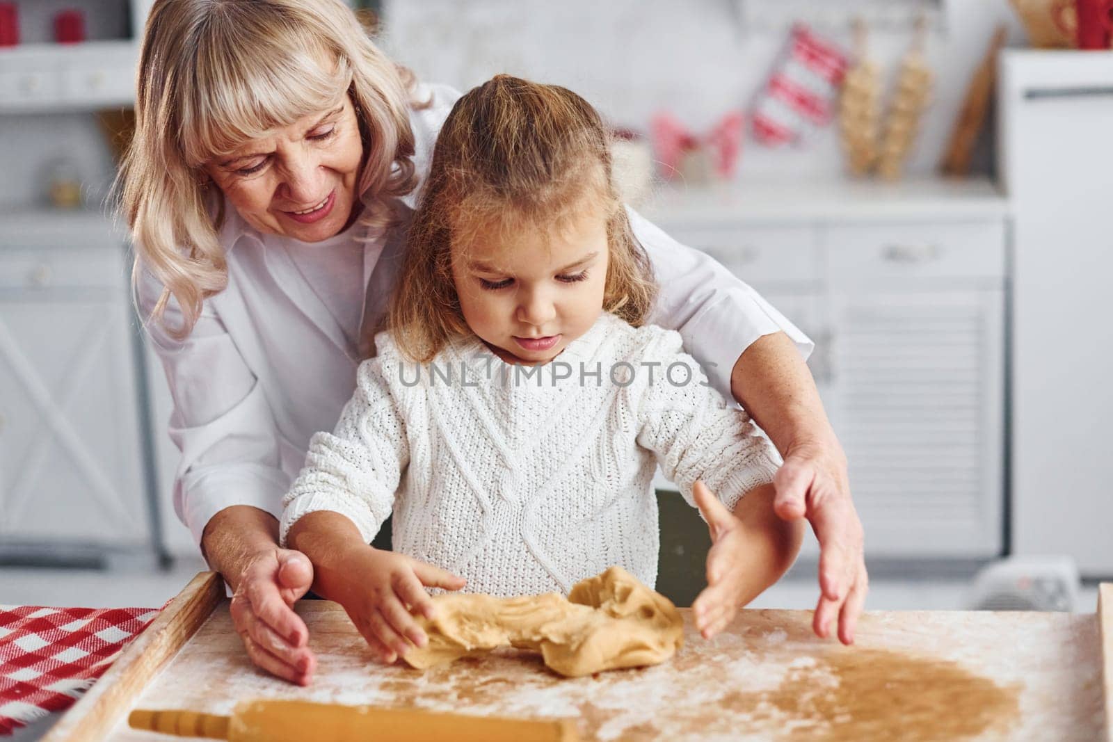 Kneads the dough. Senior grandmother with her little granddaughter cooks sweets for Christmas on the kitchen.