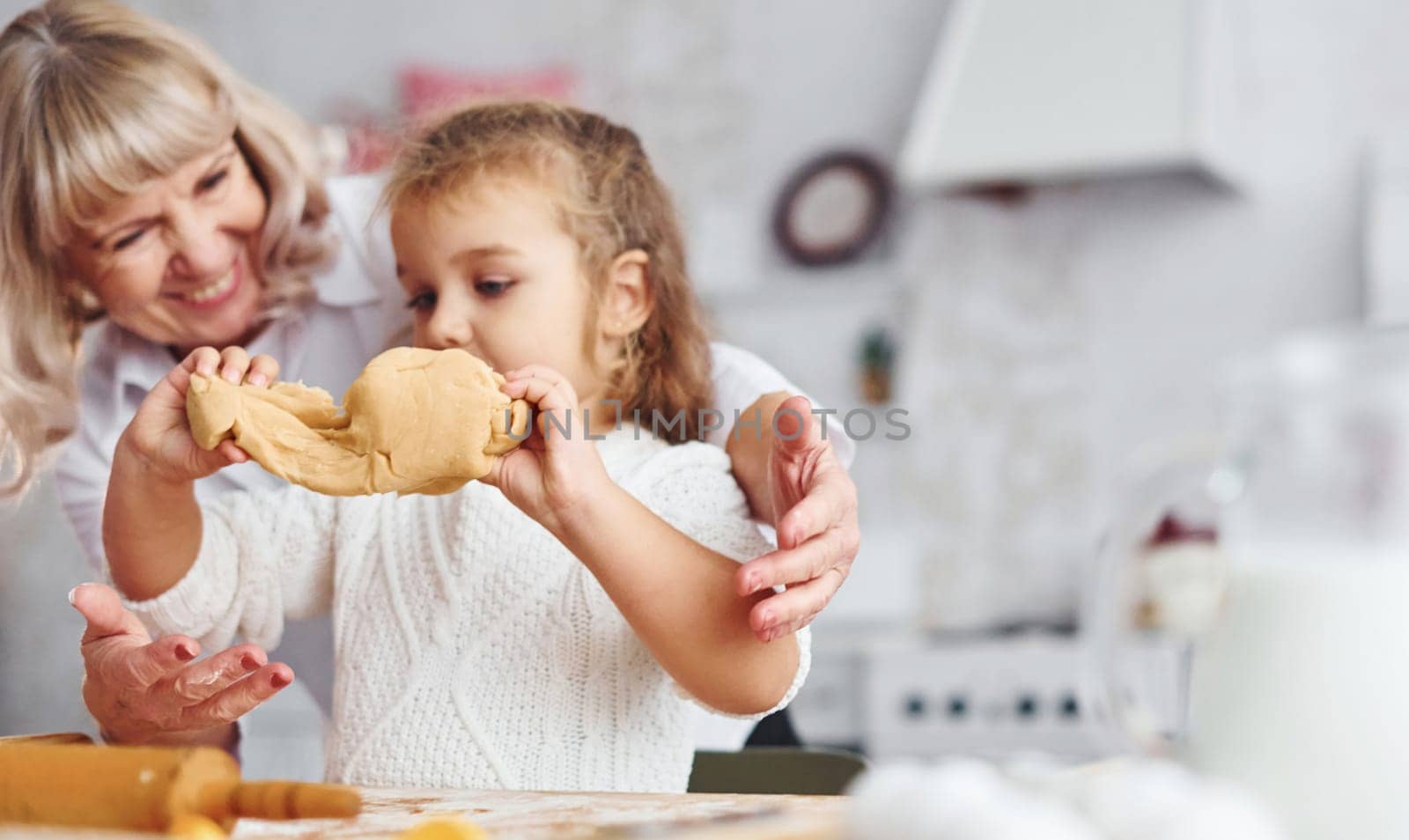 Kneads the dough. Senior grandmother with her little granddaughter cooks sweets for Christmas on the kitchen.