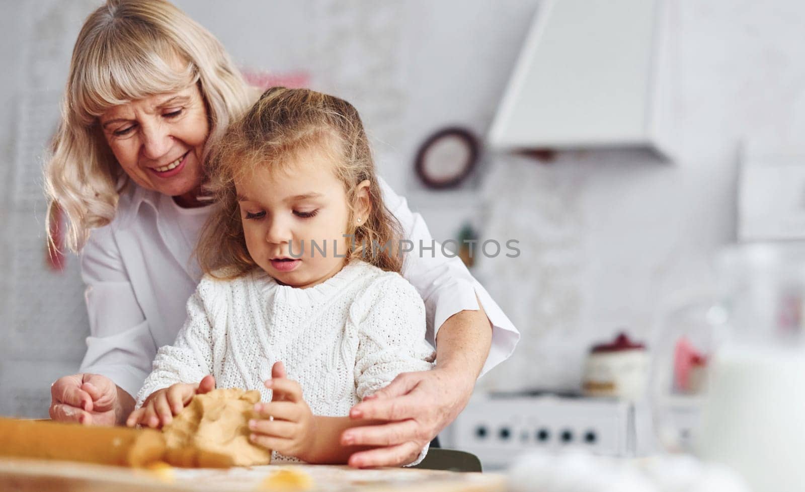 Kneads the dough. Senior grandmother with her little granddaughter cooks sweets for Christmas on the kitchen.