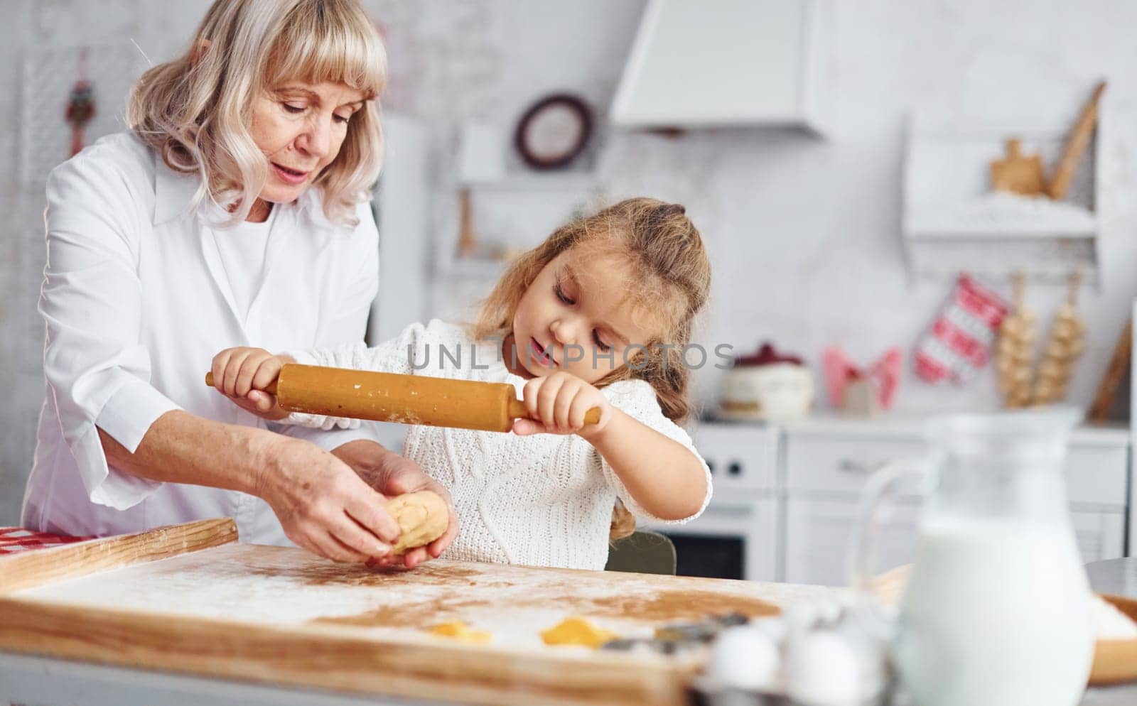Kneads the dough. Senior grandmother with her little granddaughter cooks sweets for Christmas on the kitchen.