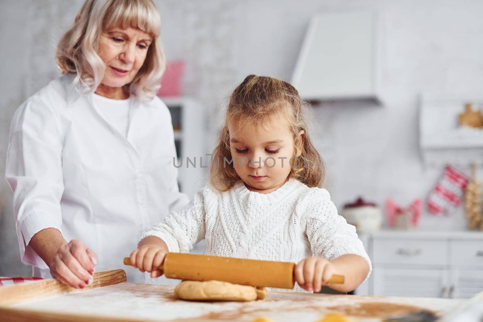 Kneads the dough. Senior grandmother with her little granddaughter cooks sweets for Christmas on the kitchen.