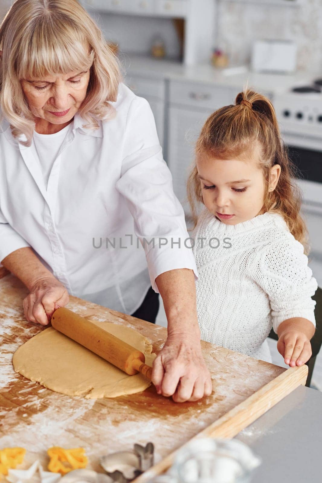 Senior grandmother with her little granddaughter cooks sweets for Christmas on the kitchen.
