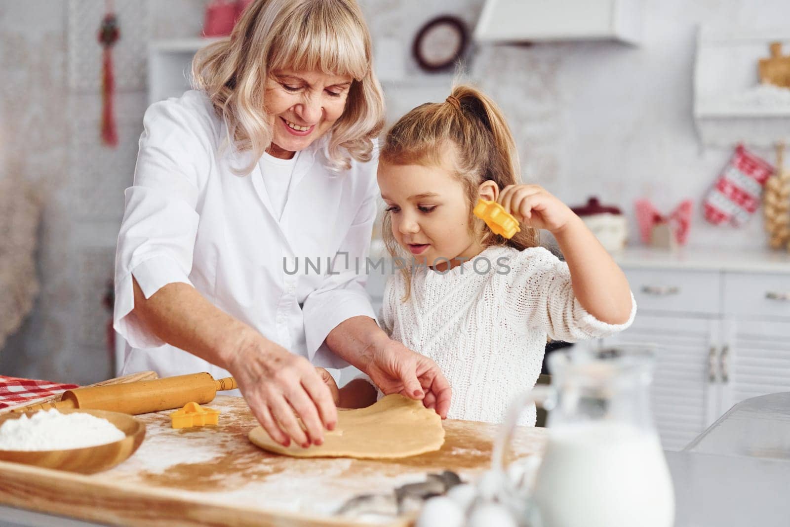 Senior grandmother with her little granddaughter cooks sweets for Christmas on the kitchen.