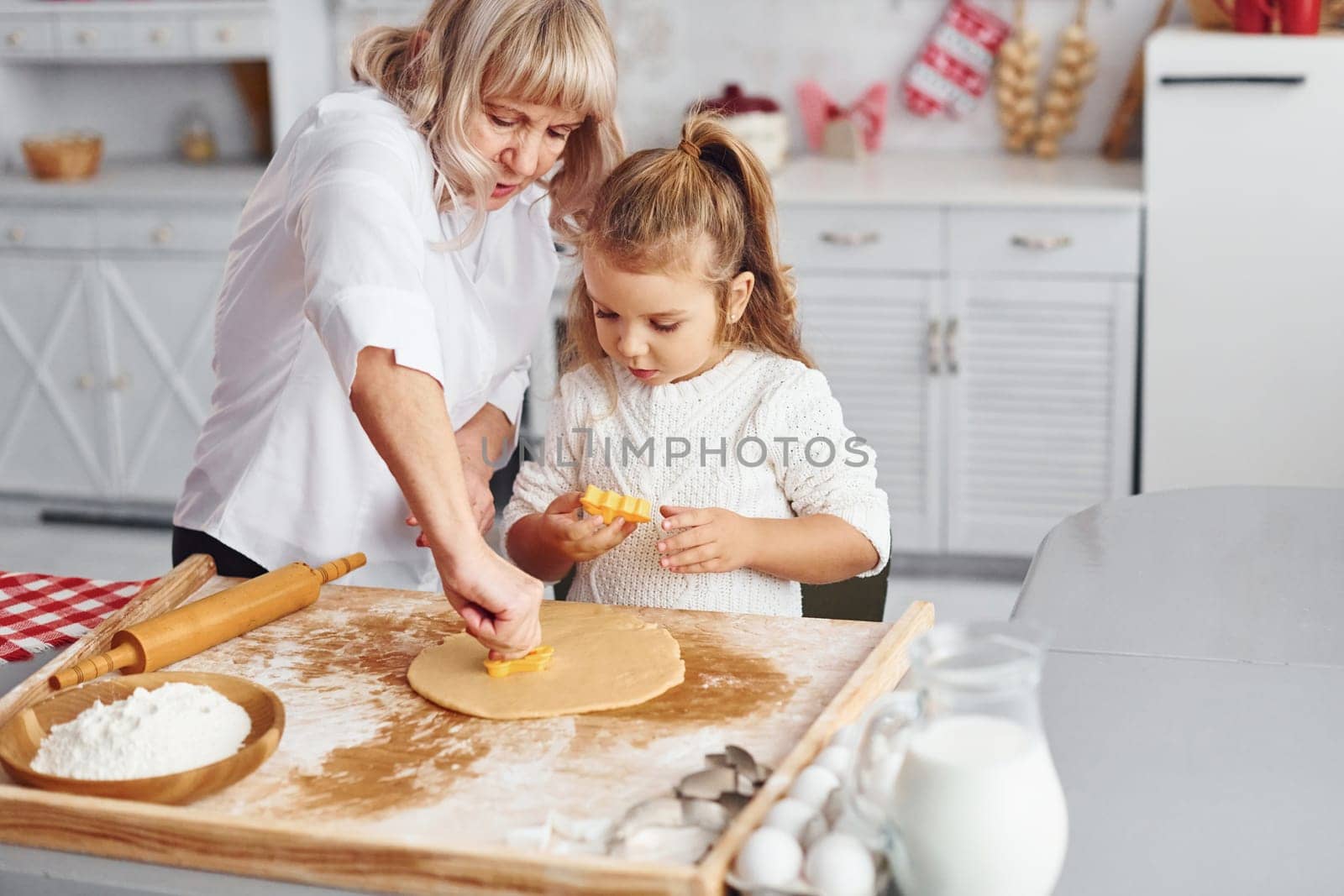 Senior grandmother with her little granddaughter cooks sweets for Christmas on the kitchen.