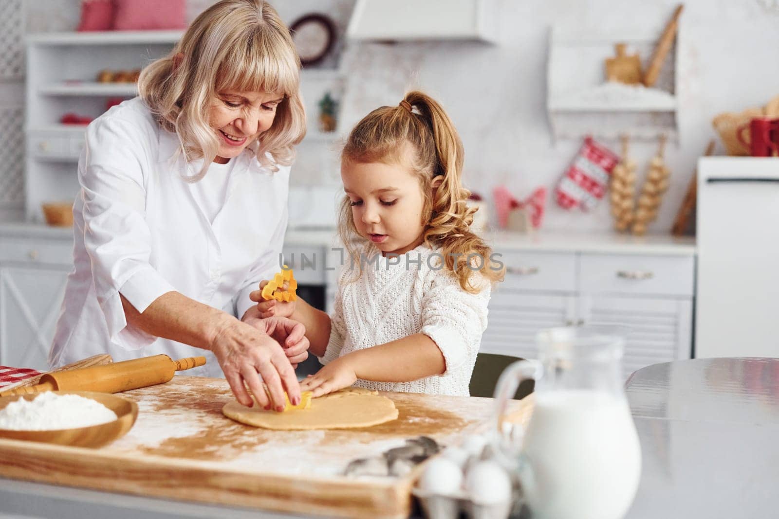 Senior grandmother with her little granddaughter cooks sweets for Christmas on the kitchen.