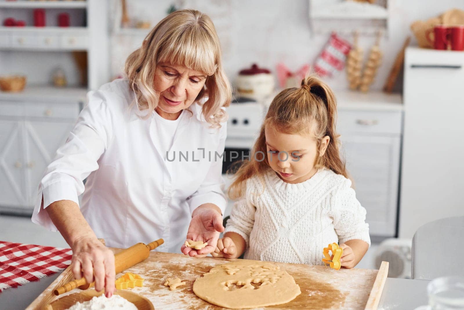 Senior grandmother with her little granddaughter cooks sweets for Christmas on the kitchen.