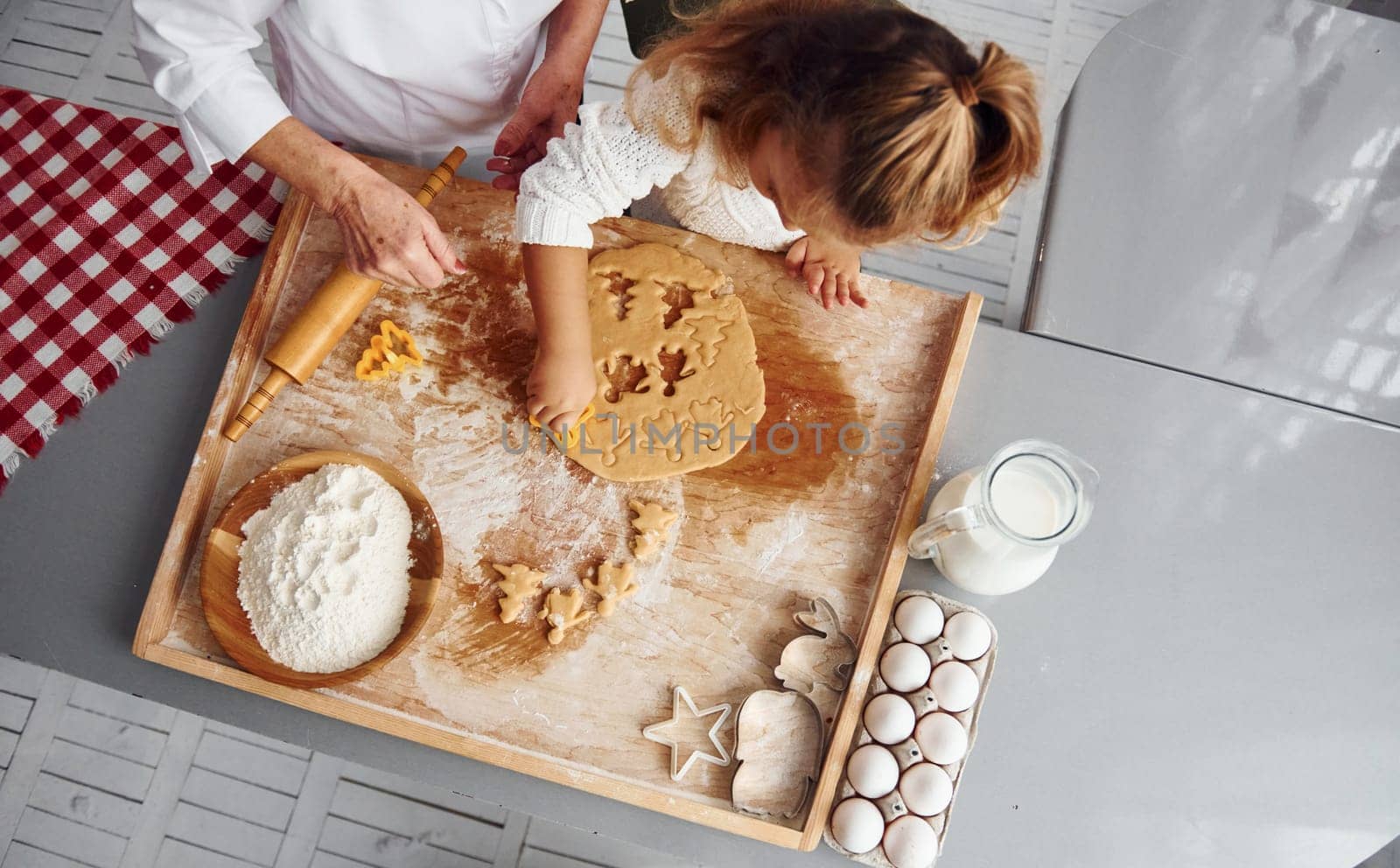 Top view of senior grandmother that with her little granddaughter cooks sweets for Christmas on the kitchen.