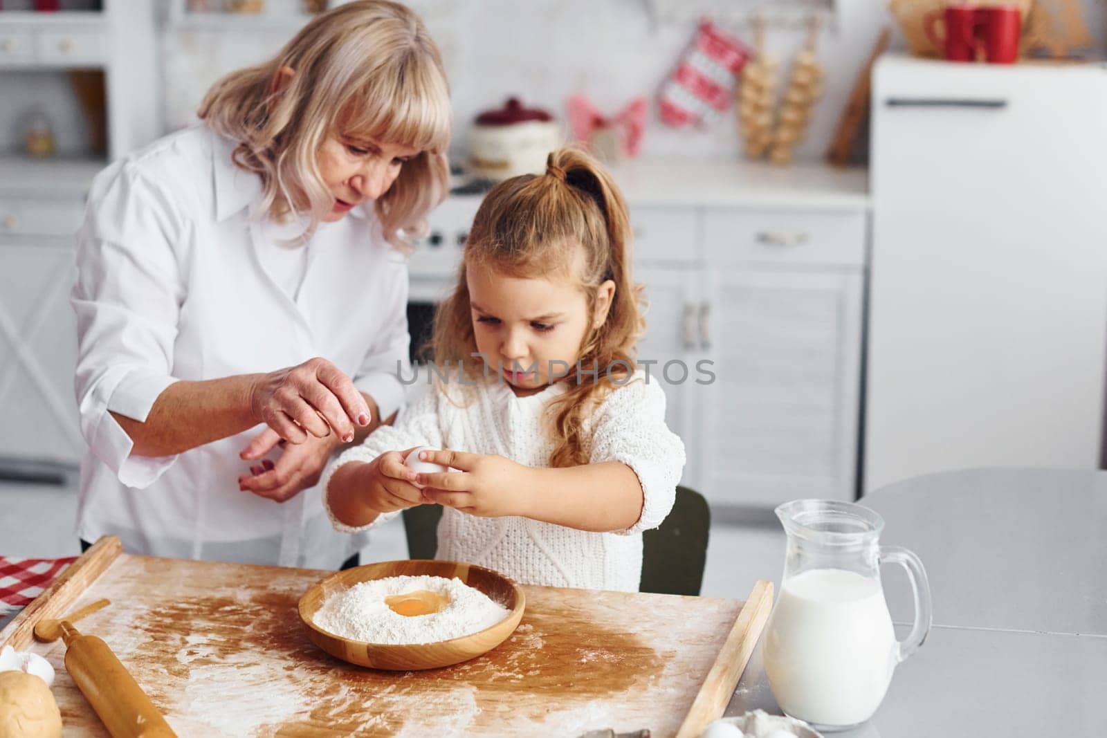 Uses eggs. Senior grandmother with her little granddaughter cooks sweets for Christmas on the kitchen.