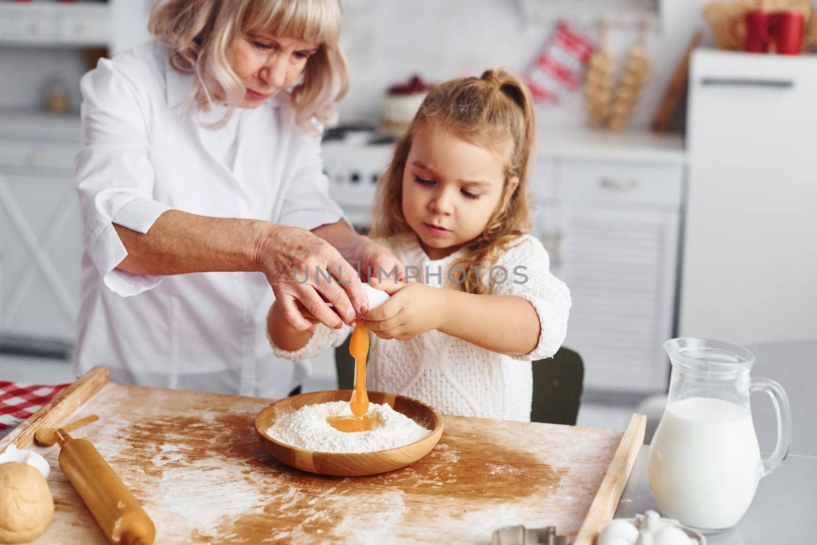 Uses eggs. Senior grandmother with her little granddaughter cooks sweets for Christmas on the kitchen.