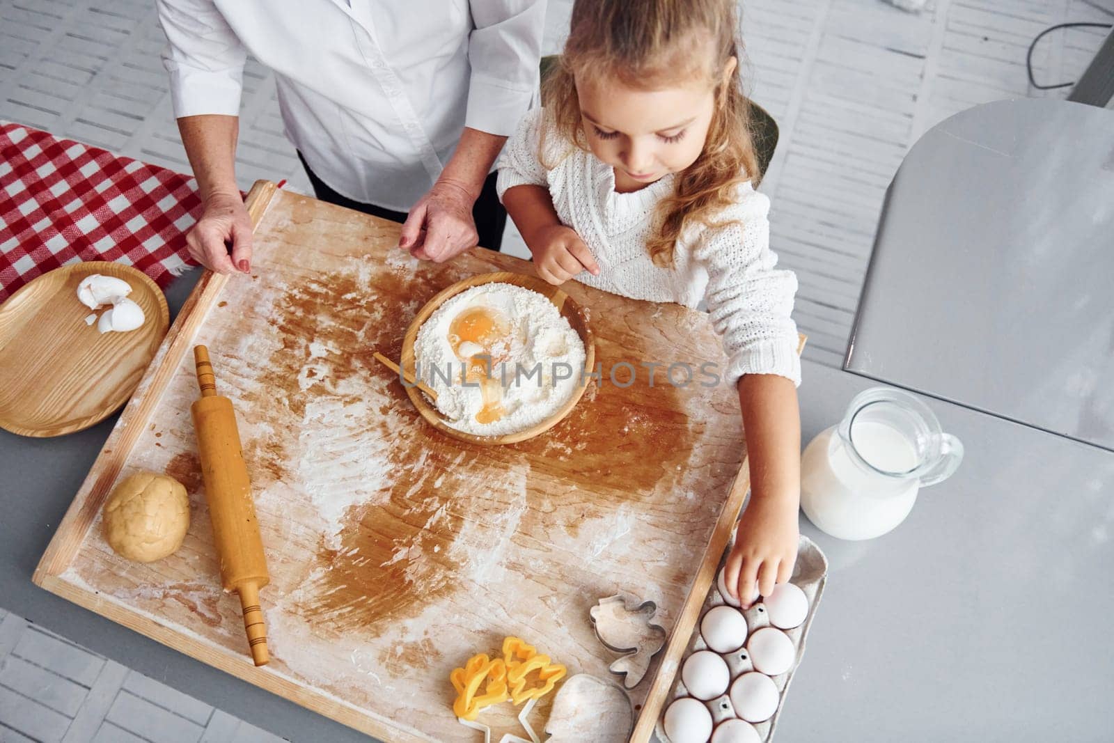 Uses eggs. Senior grandmother with her little granddaughter cooks sweets for Christmas on the kitchen.