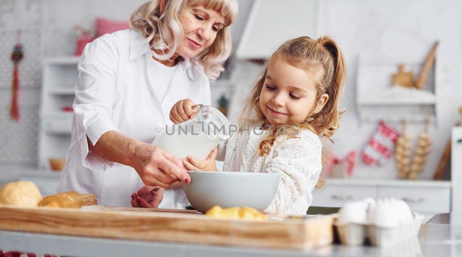 Fills with milk. Senior grandmother with her little granddaughter cooks sweets for Christmas on the kitchen.
