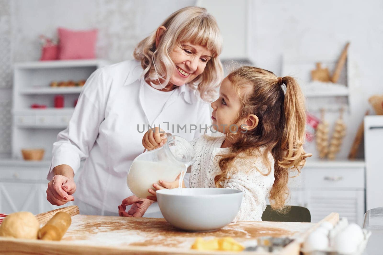 Fills with milk. Senior grandmother with her little granddaughter cooks sweets for Christmas on the kitchen.
