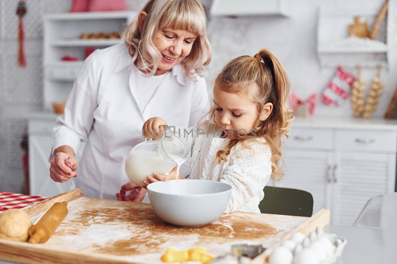 Fills with milk. Senior grandmother with her little granddaughter cooks sweets for Christmas on the kitchen.