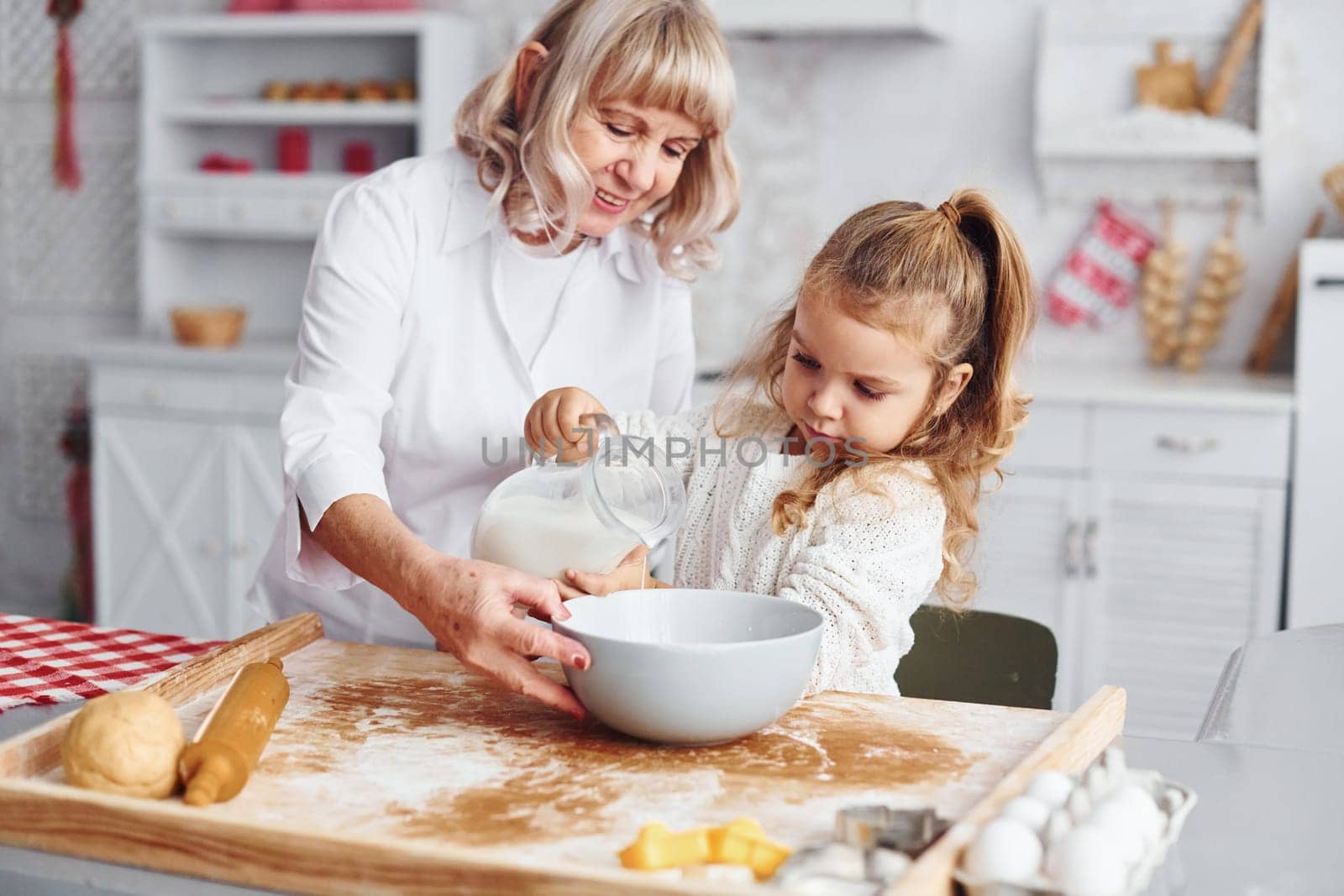 Fills with milk. Senior grandmother with her little granddaughter cooks sweets for Christmas on the kitchen.