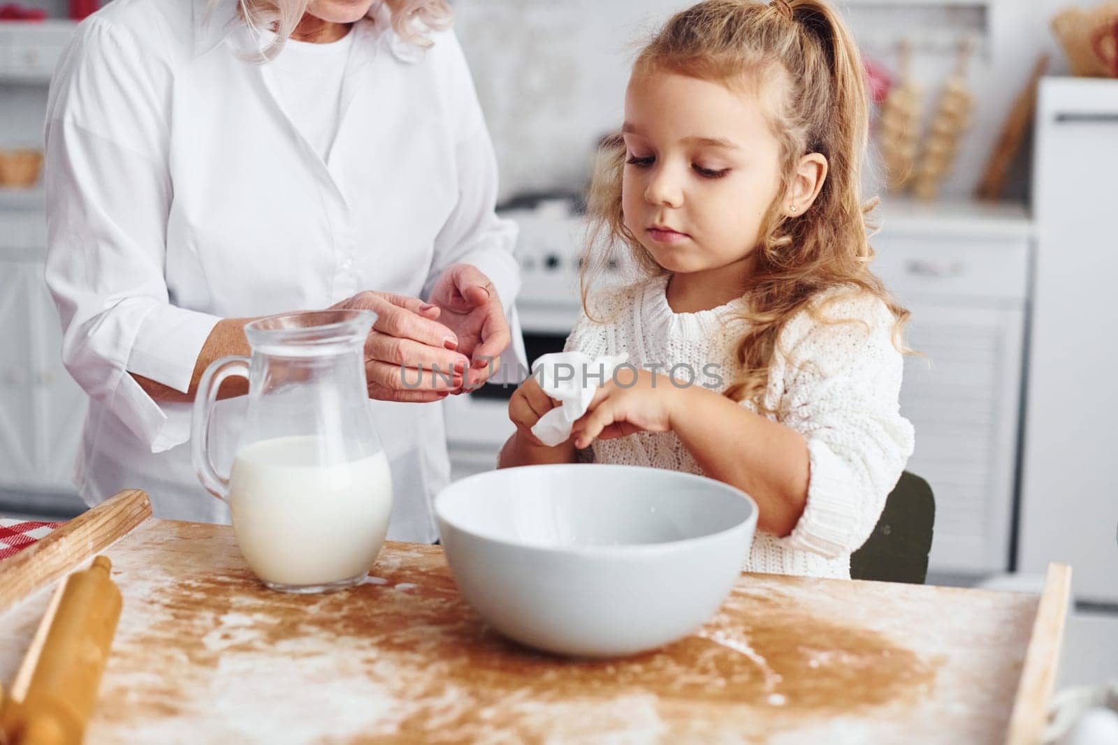 Fills with milk. Senior grandmother with her little granddaughter cooks sweets for Christmas on the kitchen.