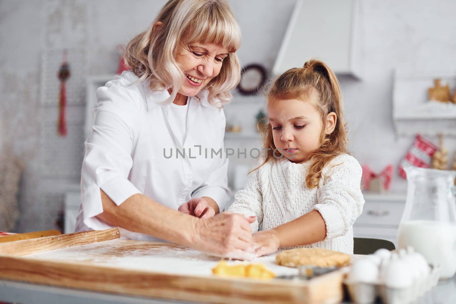 Teaching process. Senior grandmother with her little granddaughter cooks sweets for Christmas on the kitchen.