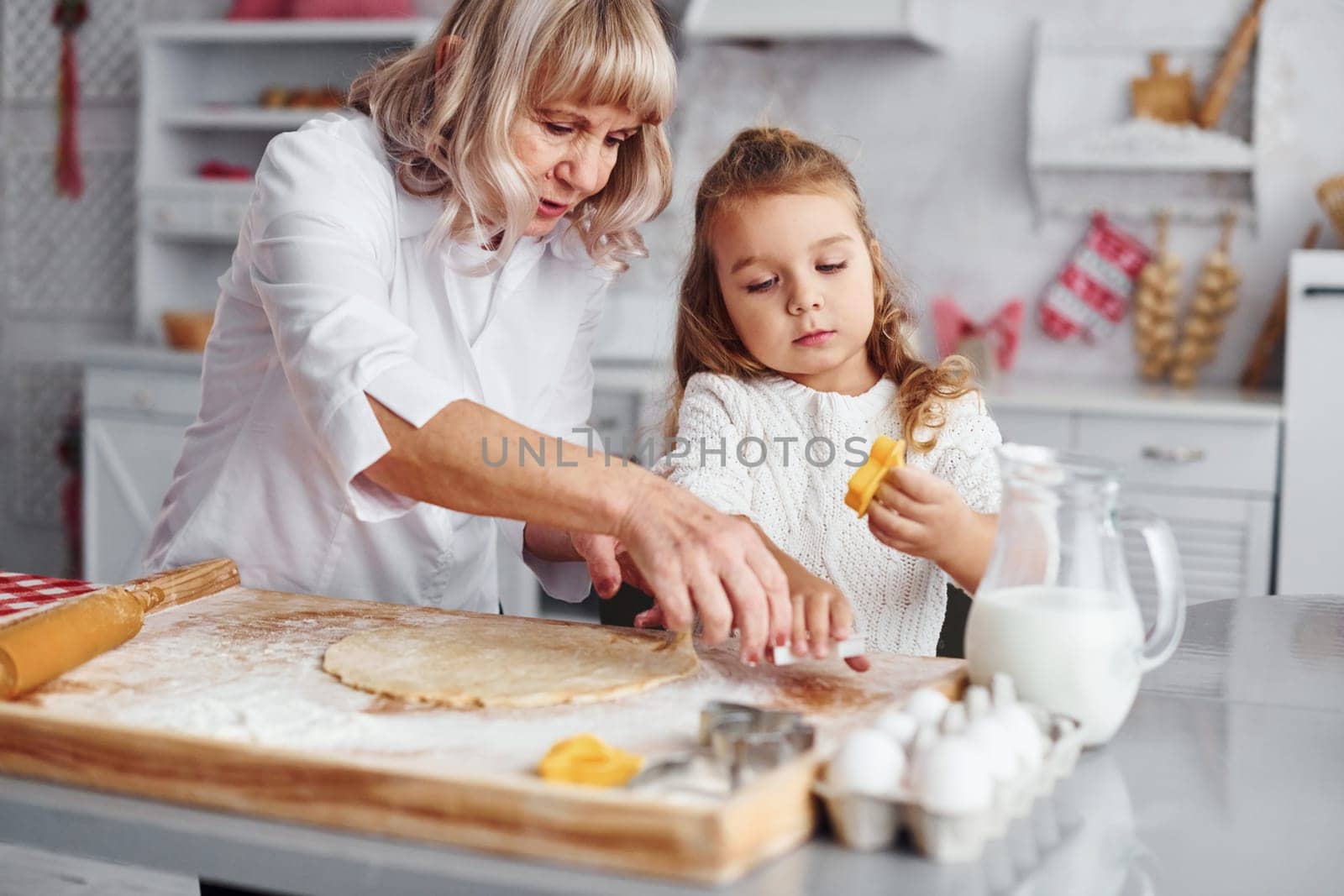 Teaching process. Senior grandmother with her little granddaughter cooks sweets for Christmas on the kitchen.