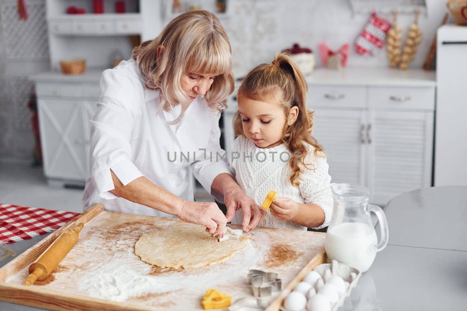 Teaching process. Senior grandmother with her little granddaughter cooks sweets for Christmas on the kitchen.