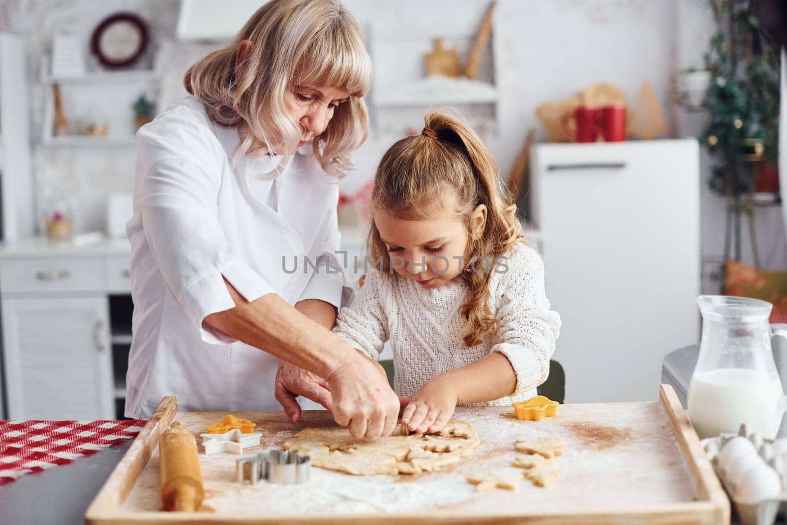 Teaching process. Senior grandmother with her little granddaughter cooks sweets for Christmas on the kitchen.