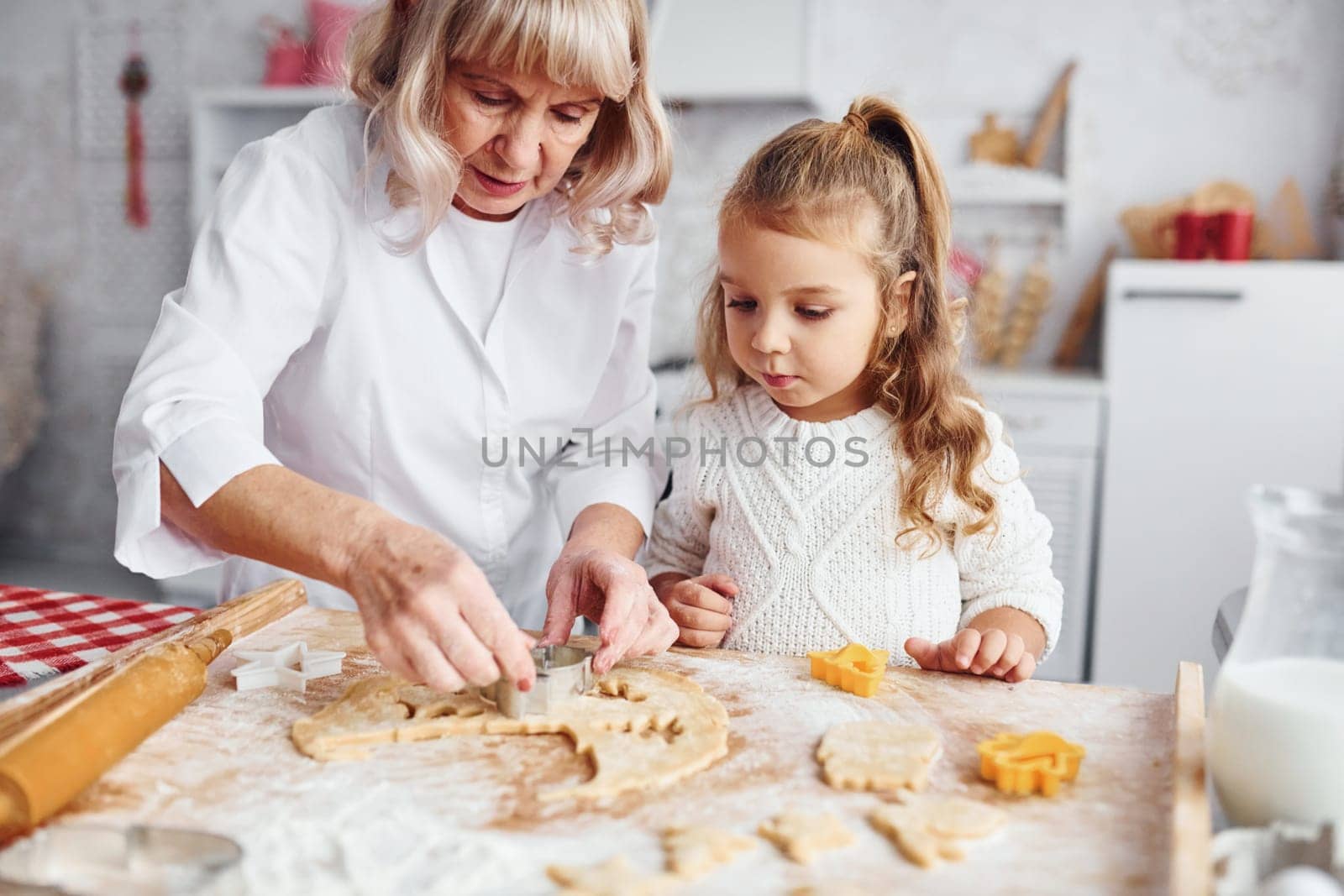 Teaching process. Senior grandmother with her little granddaughter cooks sweets for Christmas on the kitchen.