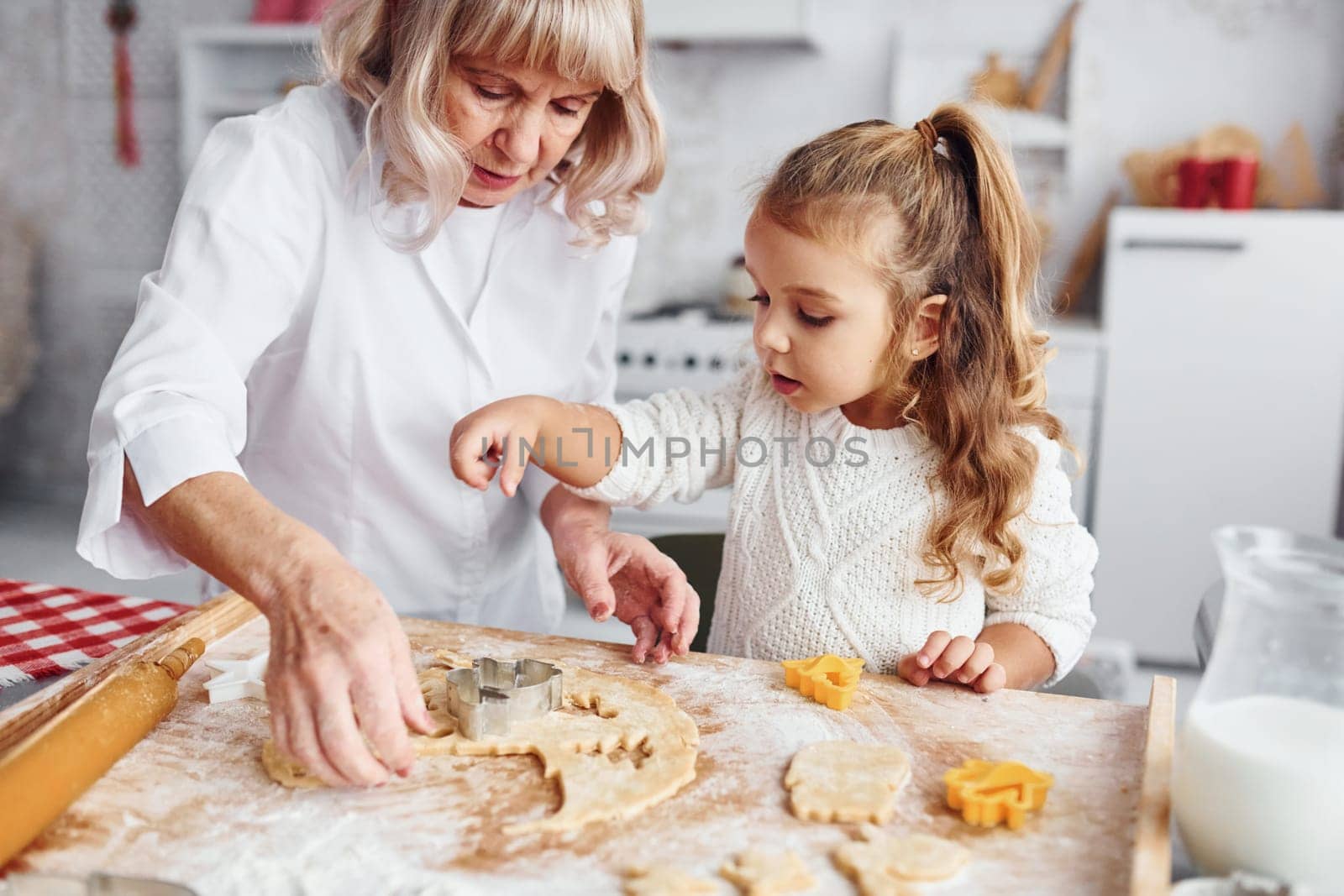 Teaching process. Senior grandmother with her little granddaughter cooks sweets for Christmas on the kitchen.