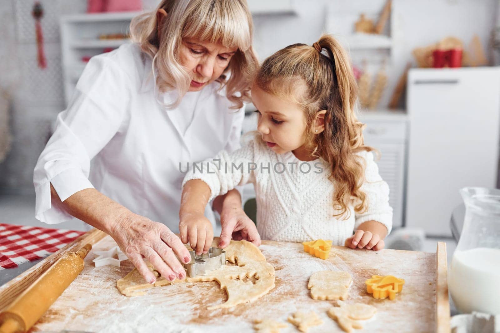 Teaching process. Senior grandmother with her little granddaughter cooks sweets for Christmas on the kitchen.
