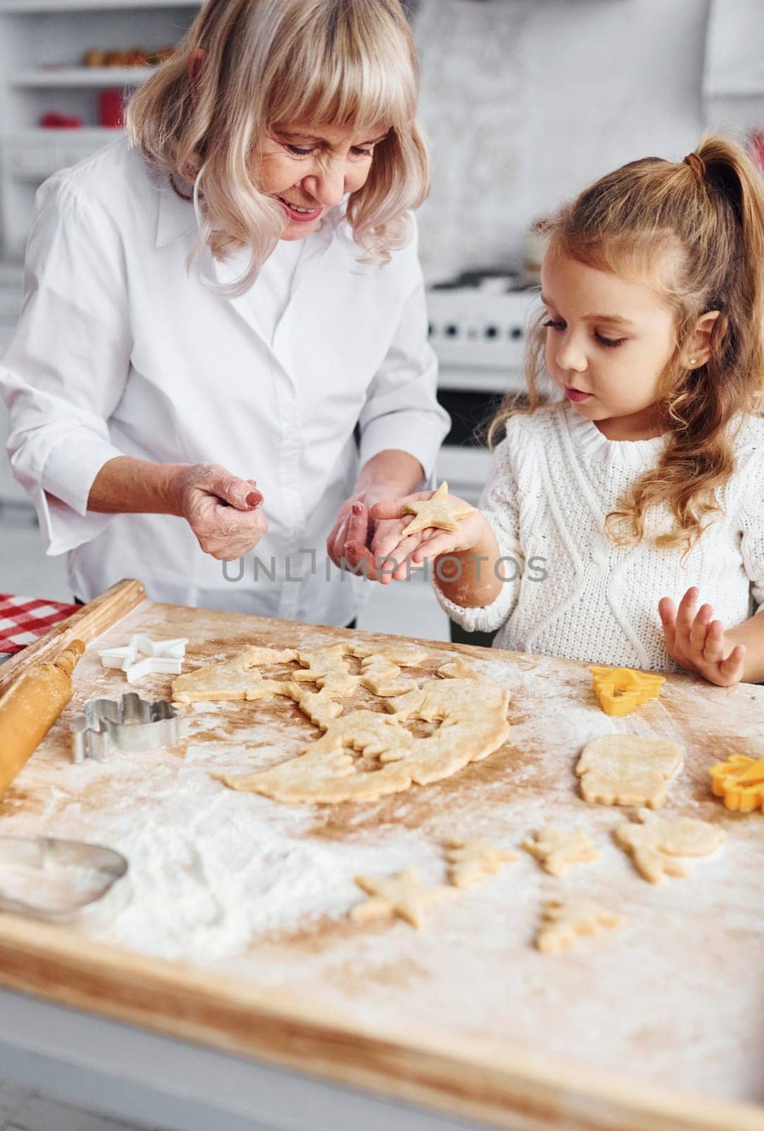 Teaching process. Senior grandmother with her little granddaughter cooks sweets for Christmas on the kitchen.