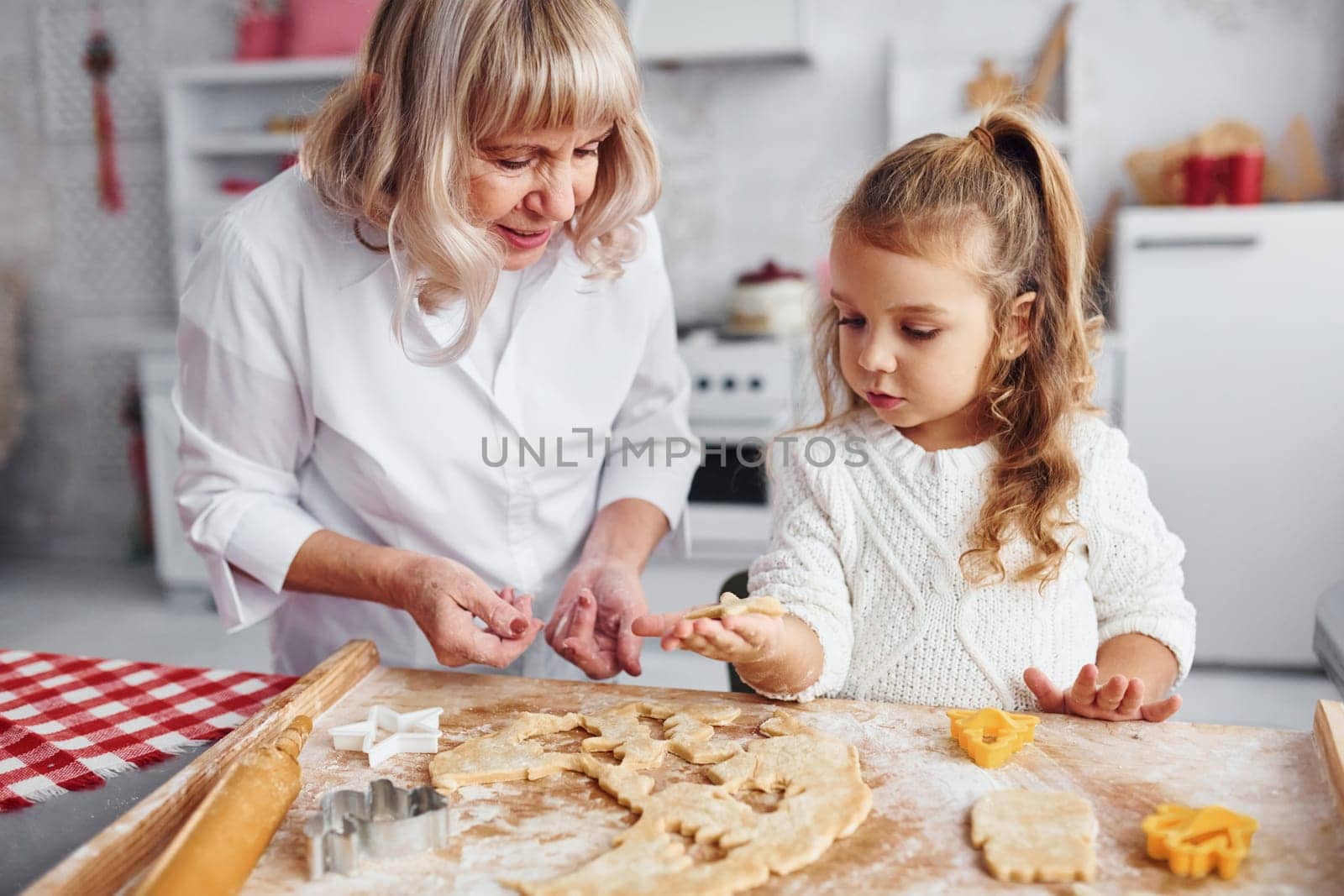 Teaching process. Senior grandmother with her little granddaughter cooks sweets for Christmas on the kitchen.